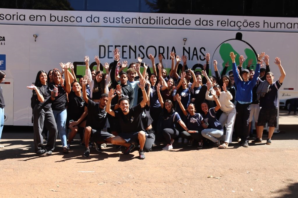 Imagem colorida de diversos estudantes à frente de um banner da Defensoria Pública do DF