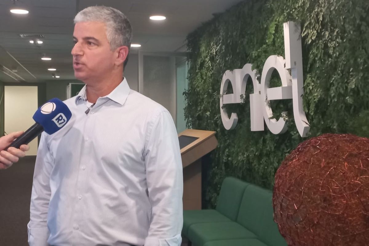 Imagem colorida de homem branco grisalho com camisa social branca. Ele fala em frente a um microfone e, ao fundo, está um letreiro escrito Enel - Metrópoles