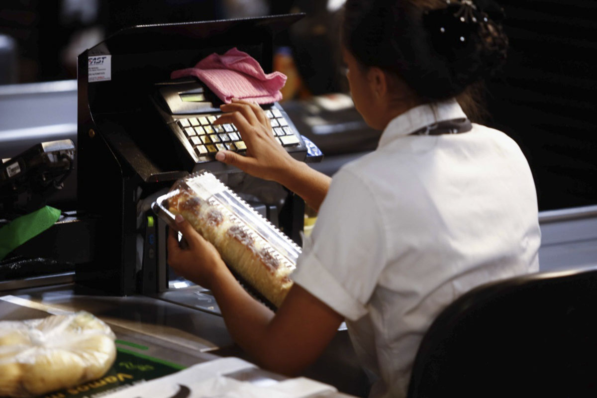 Funcionária do mercado passa o produto no caixa da loja