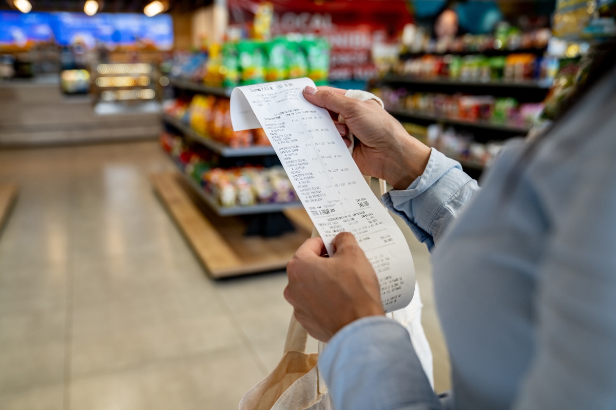 Imagem colorida, Mulher comprando em uma loja de conveniência e verificando seu recibo - Metrópoles