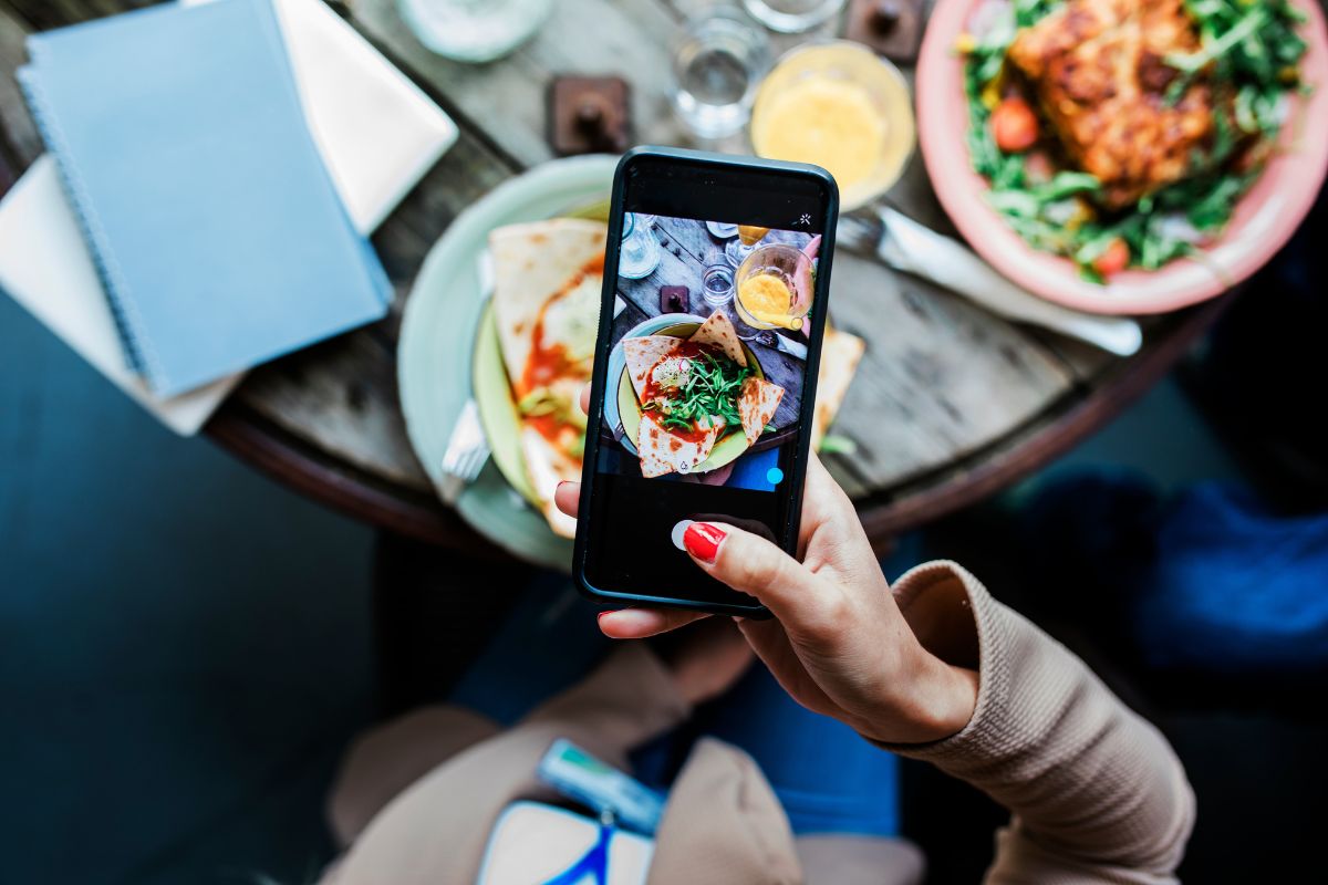 Foto colorida de uma pessoa tirando foto de um prato de comida - Metrópoles