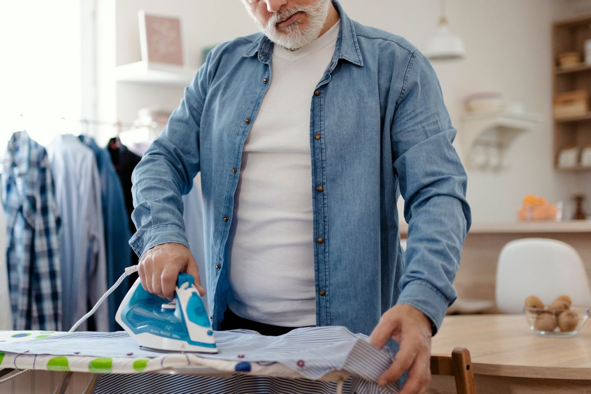 Foto colorida de um homem passando roupa - Metrópoles