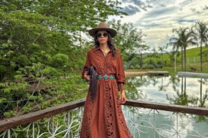 Mulher de pele clara usando vestido boho marrom, chapéu de aba reta e bolsa de franja